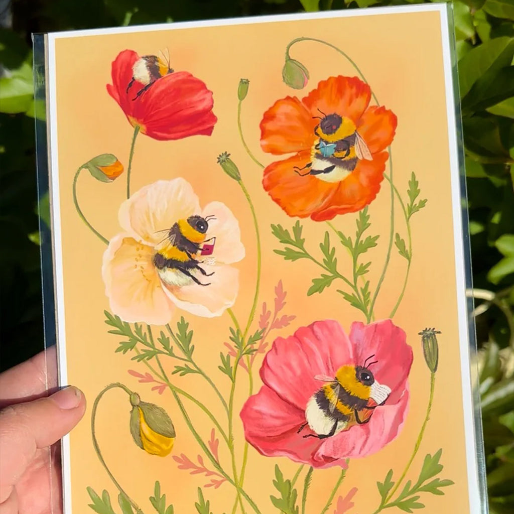 Print with colourful flowers and bees on a yellow background, held against a natural setting.