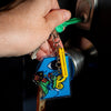 A hand holding a key with a charm keyring featuring a blue cartoon figure holding a bunch of flowers and a butterfly on a separate chain.