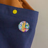 A close-up of a navy blue fabric backpack, featuring a colourful circular pin with a yellow bunny and flowers.