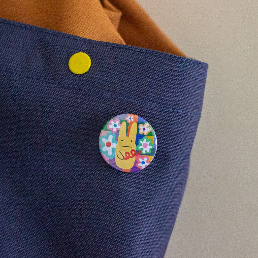 A close-up of a navy blue fabric backpack, featuring a colourful circular pin with a yellow bunny and flowers.