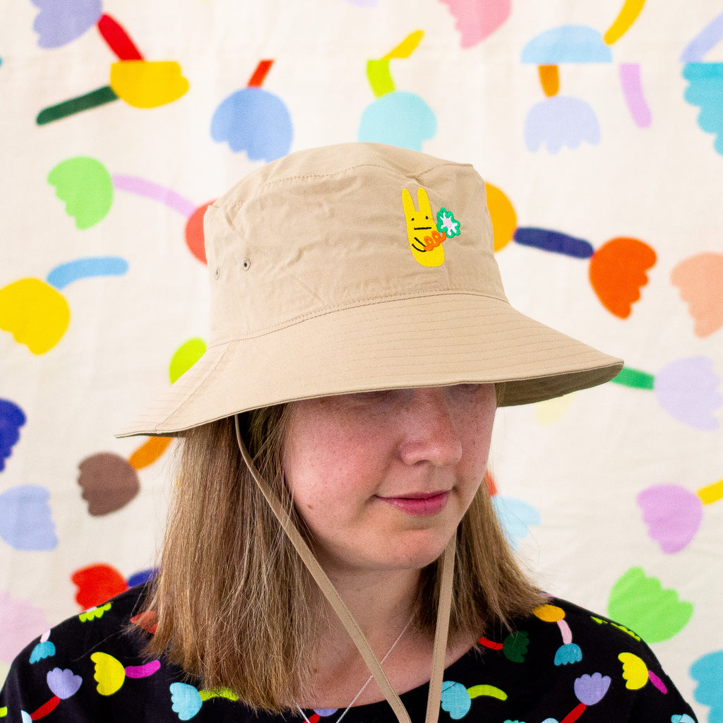 Model wearing the khaki bunny bucket hat. Embroidered yellow bunny holding a green flower. 
