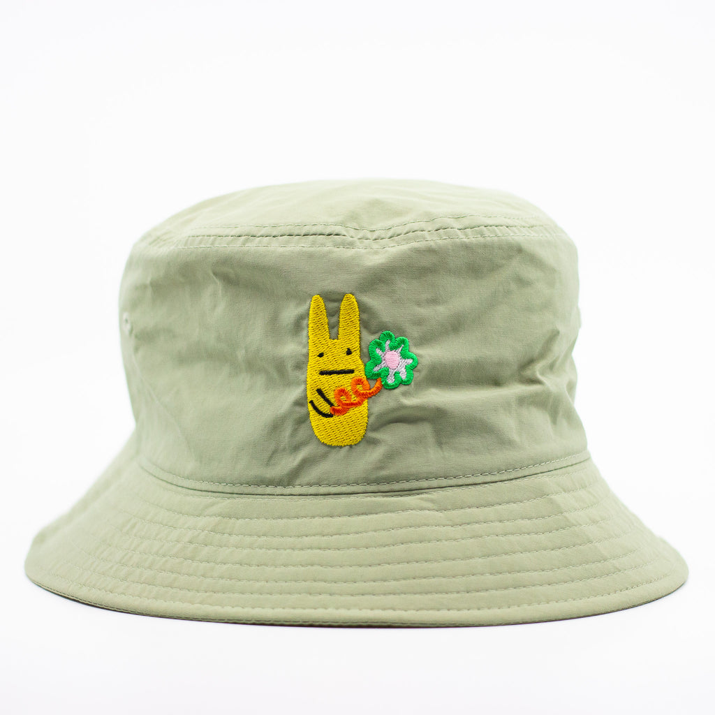 Bunny bucket hat, front view. Pistachio coloured. Add a touch of fun to your outfit with this playful bucket hat, featuring an embroidered yellow bunny character holding a large flower. Made from lightweight fabric, the brim offers stylish sun protection.