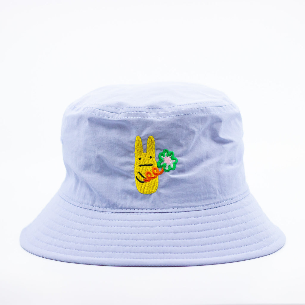 Front view of a powder blue bucket hat. With yellow embroidered bunny character holding a green clover with red stem. 