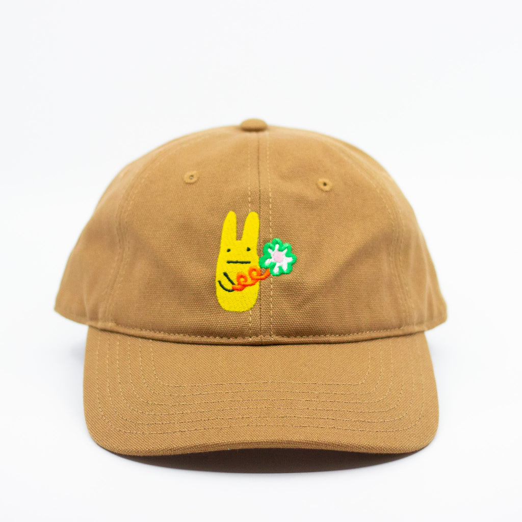 Front view of a mustard baseball cap with a yellow bunny and green clover embroidered design