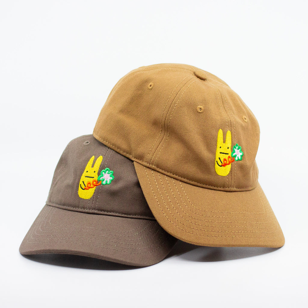 Picture of two baseball caps, mustard and dark brown, with a yellow bunny and green clover embroidered design on a white background