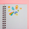 A spiral-bound notebook with a light blue and white gingham cover, decorated with colourful glittery stickers against a solid pink background.