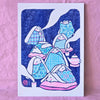A rectangular art print featuring a whimsical illustration of sleeping rabbits wrapped in patterned blankets, set against a dark blue background with white steam-like shapes. The print is displayed on a textured pink surface.