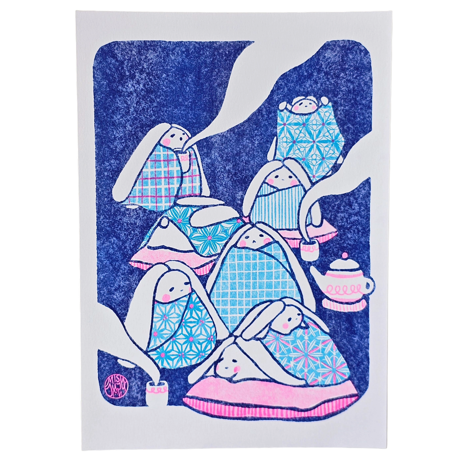 A rectangular art print featuring a whimsical illustration of rabbits wrapped in patterned blankets, set against a dark blue textured background with white abstract shapes and a small pink teapot.