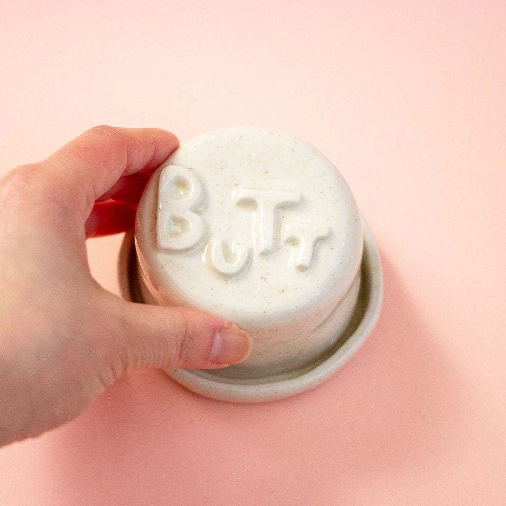 Hand holding a lid with 'BUTT' on a peach background