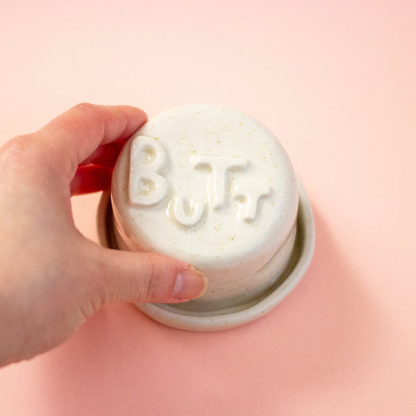 Hand holding a lid with 'BUTT' on a peach background