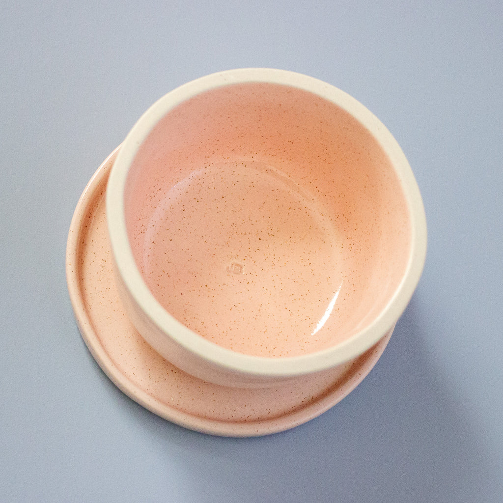 Pink ceramic bowl on a matching pink saucer against a light blue background
