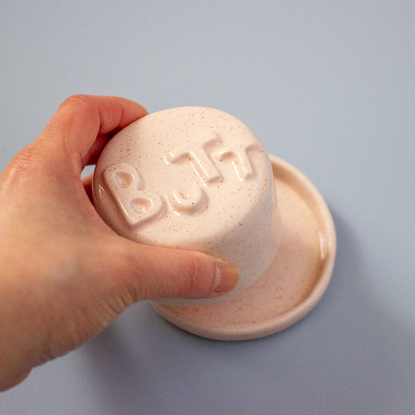 Hand holding a pink object with 'BUTT' printed on it against a blue background
