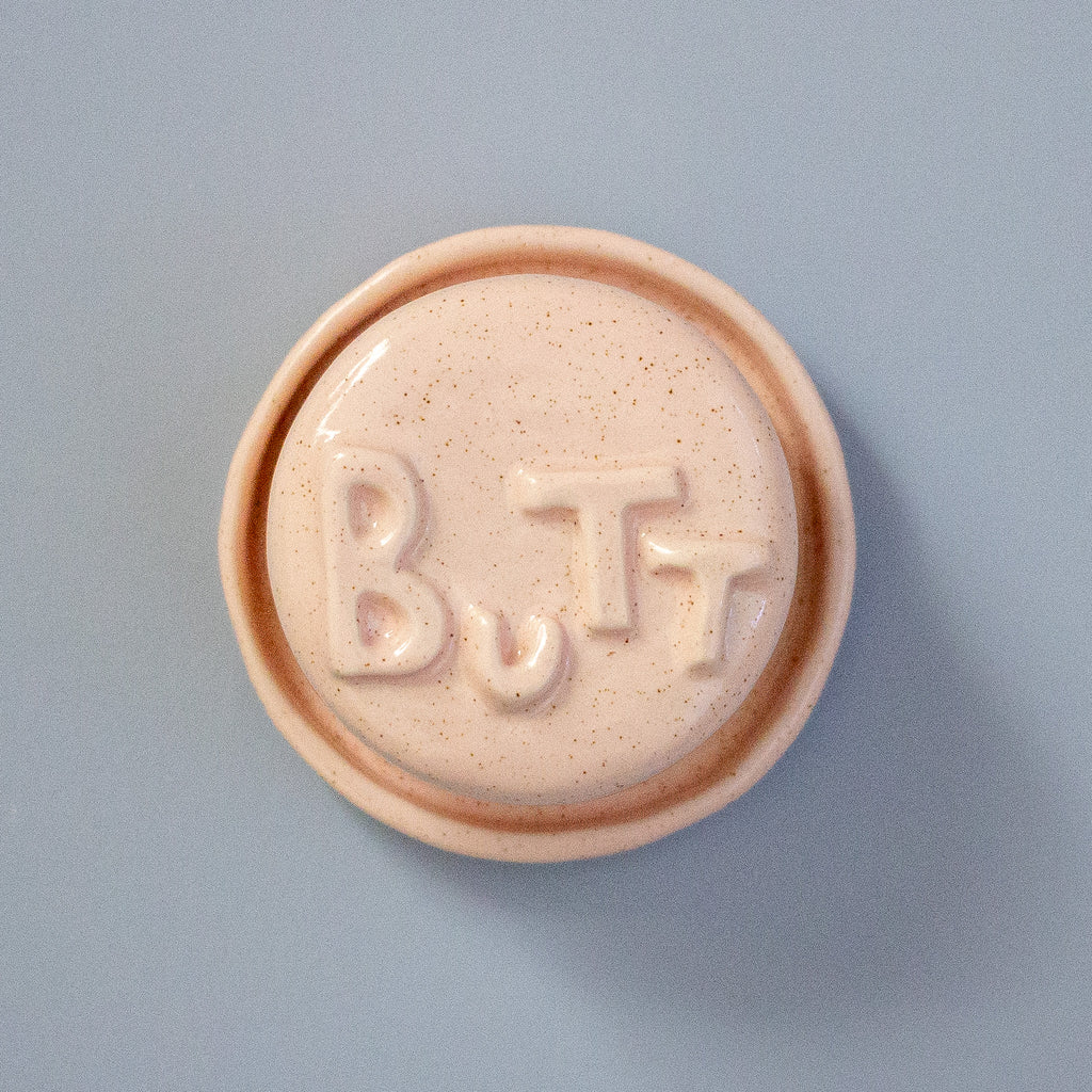 Round pink object with 'BUTT' embossed on a light blue background