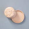 Round pink container with 'BUTT' text on a light blue background