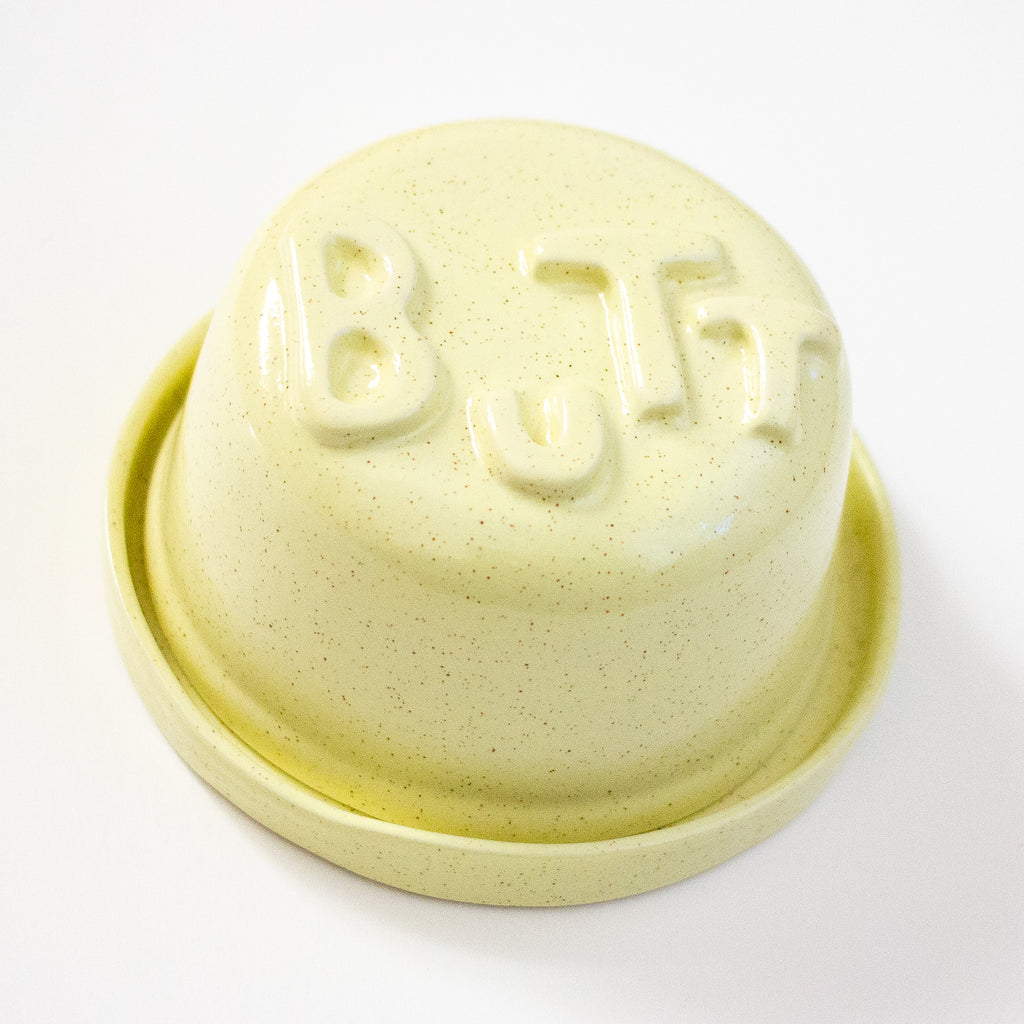 Yellow ceramic butter dish with 'BUTT' letters on a white background