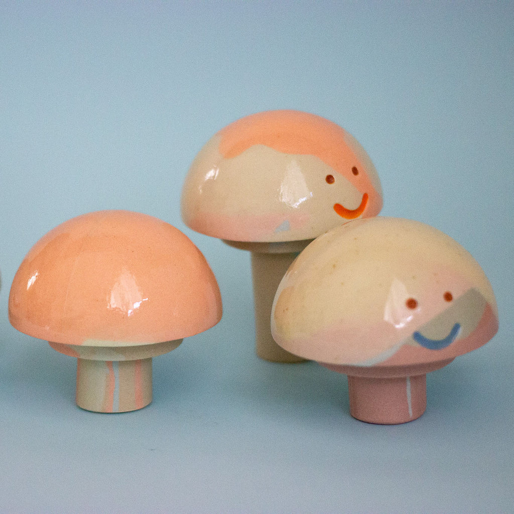 Three ceramic mushrooms with smiling faces on a light blue background