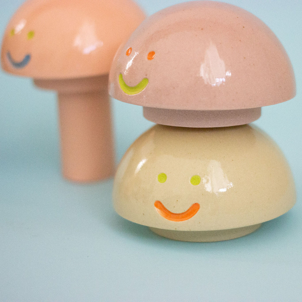 Three ceramic mushroom-shaped figurines with smiling faces on a light blue background