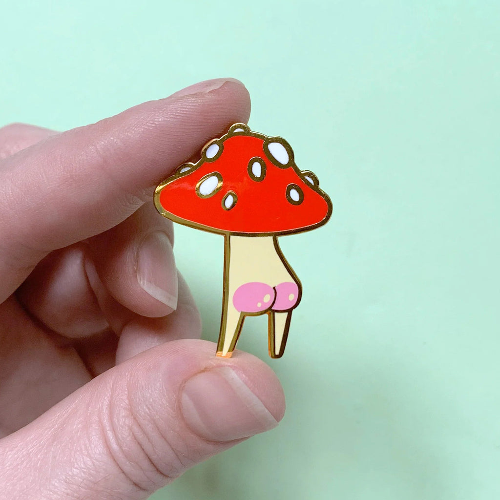 Hand holding a mushroom-shaped pin against a light green background