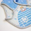A close-up of a textured baby bib in light blue and white, featuring a cartoon cat wearing a yellow hat and a striped border.