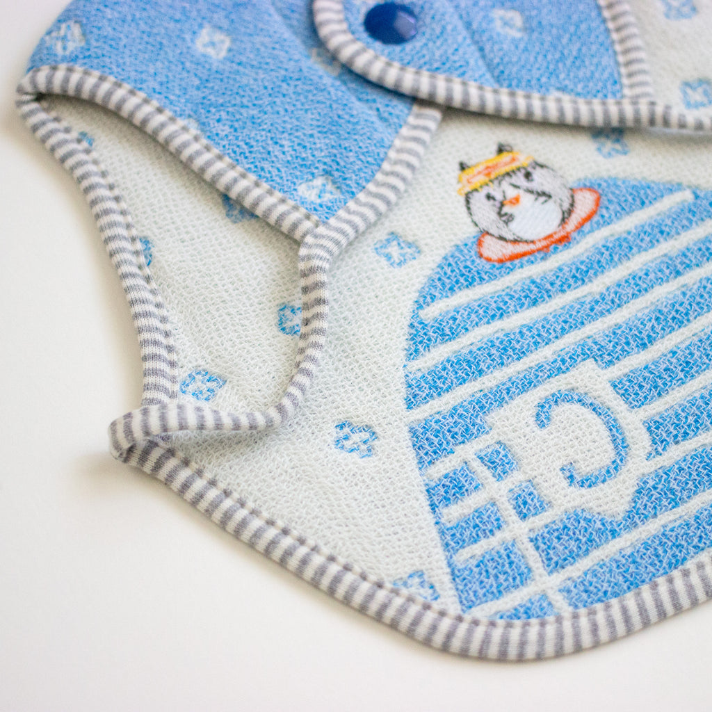A close-up of a textured baby bib in light blue and white, featuring a cartoon cat wearing a yellow hat and a striped border.