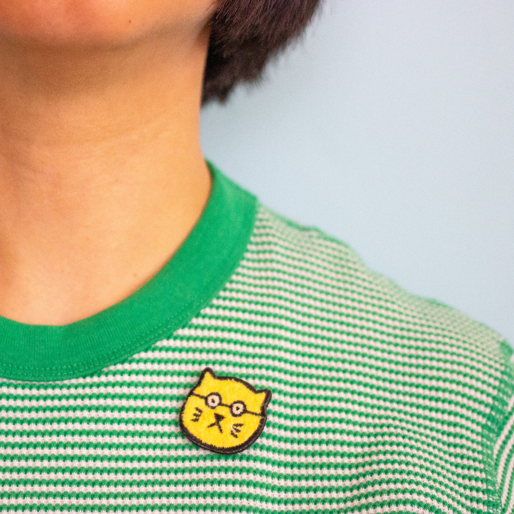 Green and white striped shirt with a yellow cat patch on a light blue background