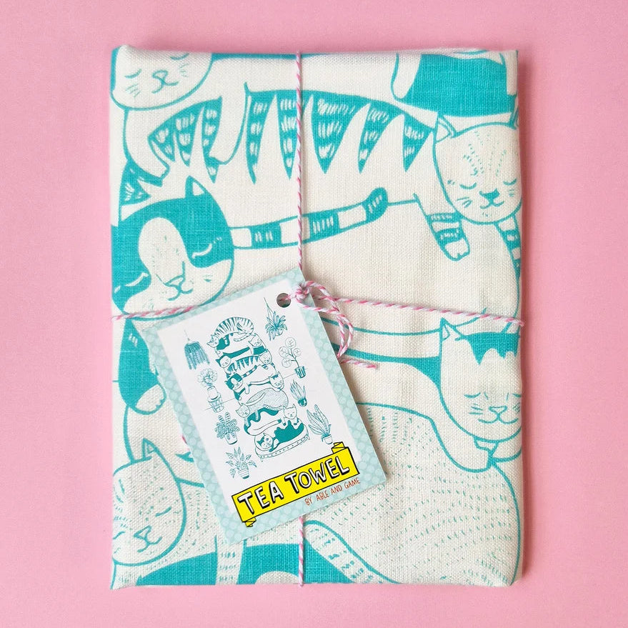 Tea towel with cat pattern and matching tag on a pink background