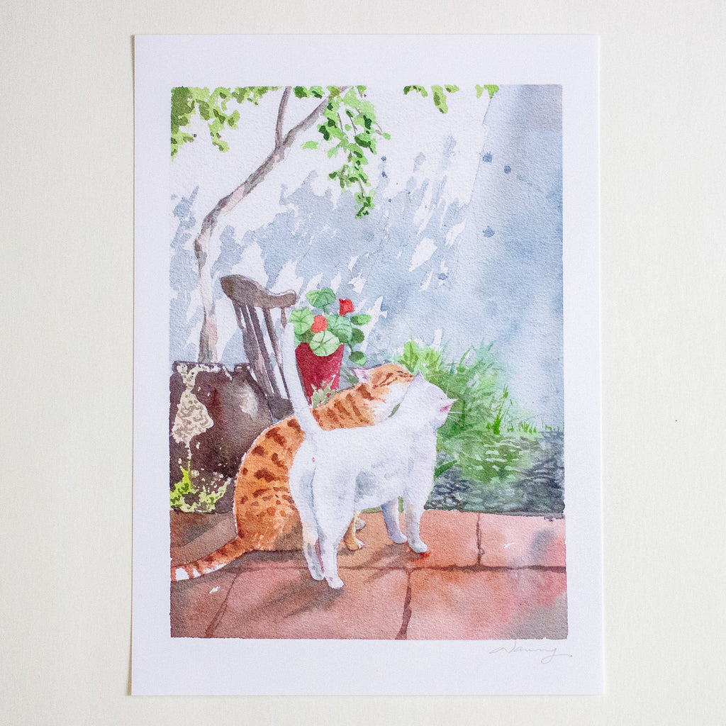 A watercolour art print depicting an orange and white cat standing on a tiled patio next to a potted plant, with a wooden chair and tree in the background. The print is presented on a white paper sheet against a light beige background.