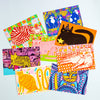A set of colourful illustrated postcards featuring whimsical cat designs, arranged overlapping on a light blue background.