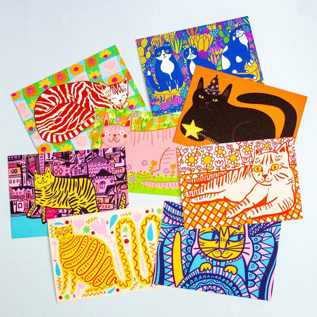 A set of colourful illustrated postcards featuring whimsical cat designs, arranged overlapping on a light blue background.