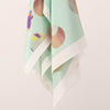 Hanging view of the changing sky scarf. Screen printed round elements with quirky lines and shapes over a light mint background. 