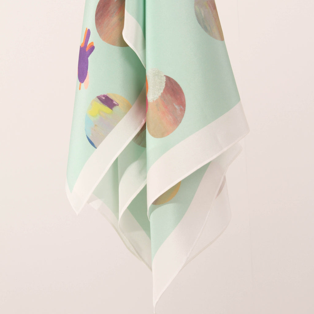 Hanging view of the changing sky scarf. Screen printed round elements with quirky lines and shapes over a light mint background. 