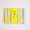 A folded Japanese cotton tea towel with a yellow and green floral pattern, wrapped in a bright yellow paper band with Japanese calligraphy and a Kontex brand label, set against a plain white background.