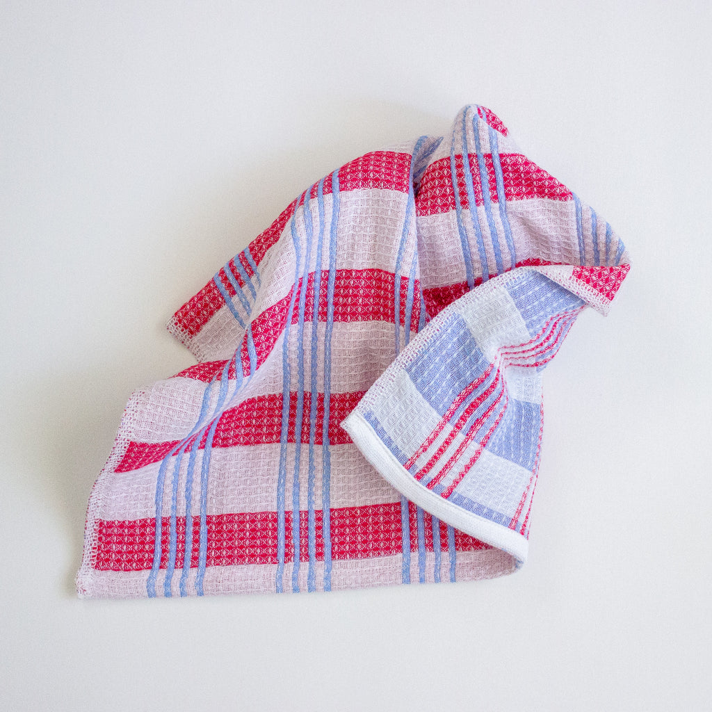 A folded waffle-weave kitchen towel with a pink, red, and light blue plaid pattern, displayed on a clean white background.