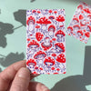 Rectangular sticker with red mushroom pattern held by a hand against a light blue background