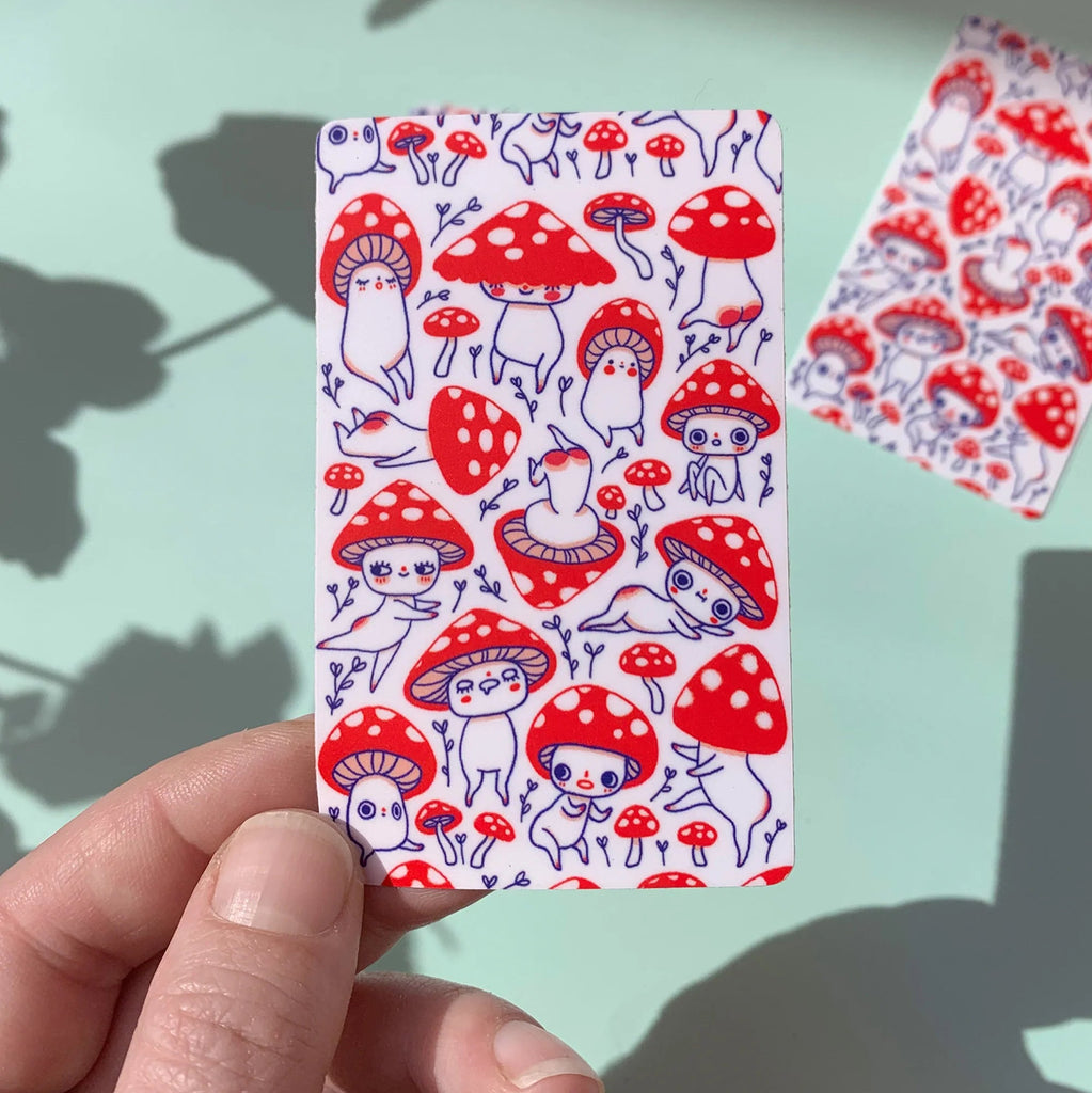 Rectangular sticker with red mushroom pattern held by a hand against a light blue background