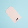 A light pink paper hang tag with a hole at the top left, printed with the brand name 'shuh.' and website 'www.shuh.com'