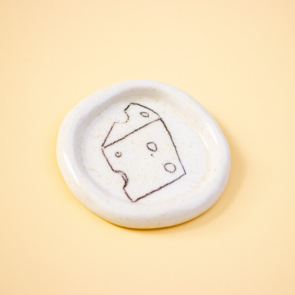 Round ceramic dish with a cheese illustration on a yellow background