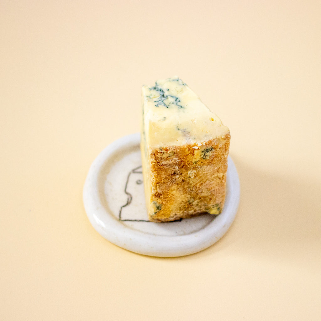 Block of blue cheese on a dish with a yellow background