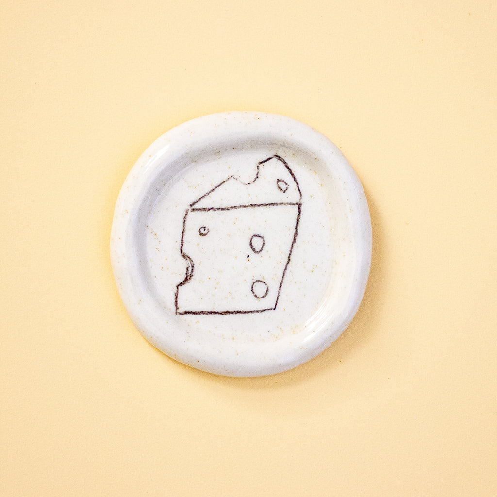Small white ceramic dish with a piece of cheese illustration on a yellow background