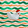 White ceramic chicken figurine on a wavy striped background with green and orange lines.