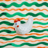White ceramic chicken figurine on a background with green and orange wavy lines