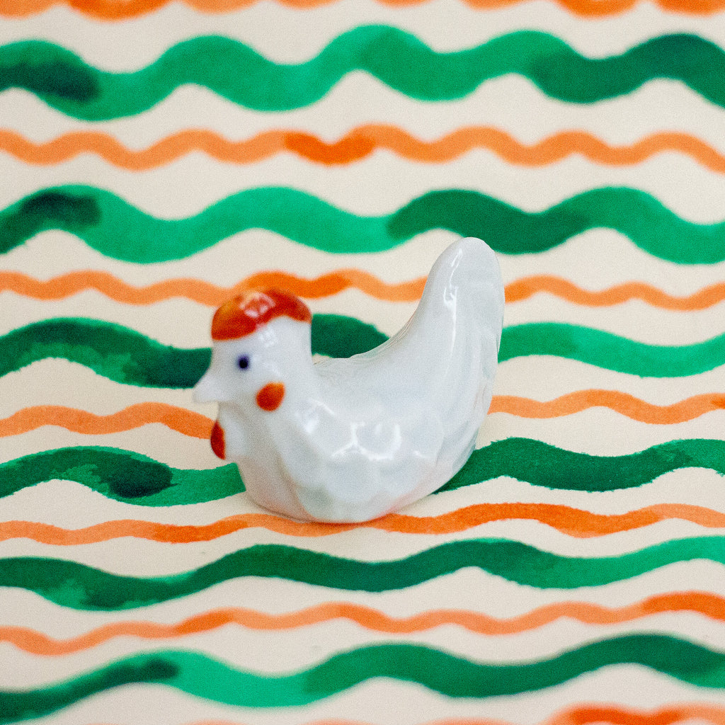 White ceramic chicken figurine on a background with green and orange wavy lines