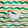 White ceramic chicken figurine on a background with green and orange wavy lines