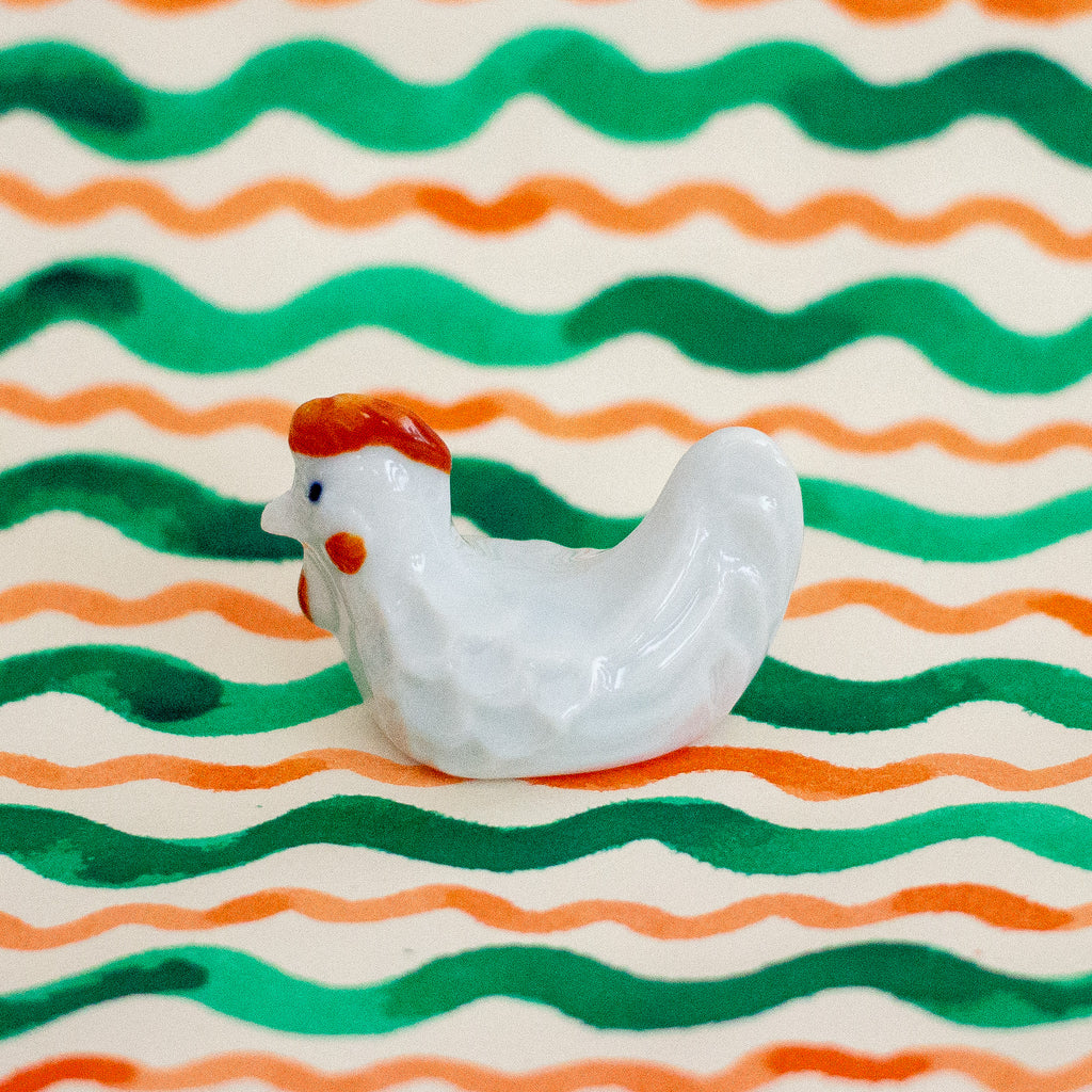 White ceramic chicken figurine on a background with green and orange wavy lines