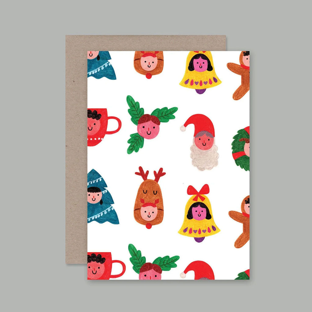 A greeting card with a white background and a colourful Christmas-themed pattern of illustrated characters, shown with a brown kraft envelope behind it on a plain grey background.
