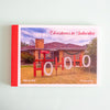 A set of postcards titled "Christmas in Suburbia" by Warren Kirk, shown standing upright against a pale mint background. The package has a red spine/border and the front features a photograph of a suburban house with large red and white "HOHOHO" lettering in the front yard.