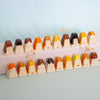 A set of small decorative ceramic vases shaped like stylised faces with short hair, arranged in two rows on a pale pink block against a light blue background. The vases have cream bases and hair in shades of orange, yellow, brown, and dark brown, with small dried flowers placed on top.