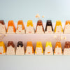 A set of hand-painted ceramic vases shaped like stylised faces with colourful hair, arranged in two rows on a light surface against a pale blue background.
