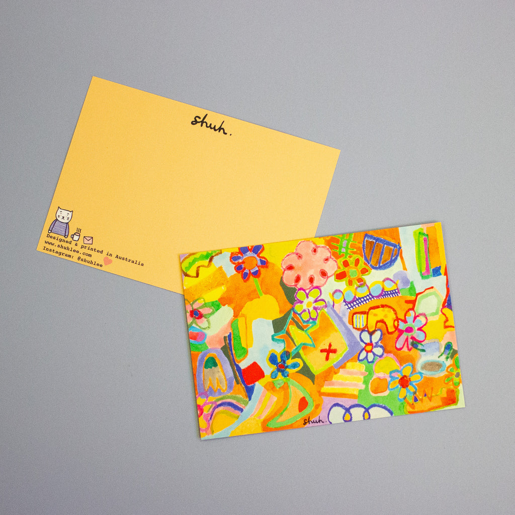 A colourful illustrated postcard on top and bottom postcard shows the back design on a neutral grey background. The postcard features a vibrant, playful doodle-style illustration, while the postcard underneath shows the back design with the logo 'shuh.' on top. 