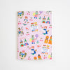 A pink notebook with a whimsical cartoon pattern of cats, cherries, and characters holding 'THANK YOU!' signs, photographed against a clean white background.